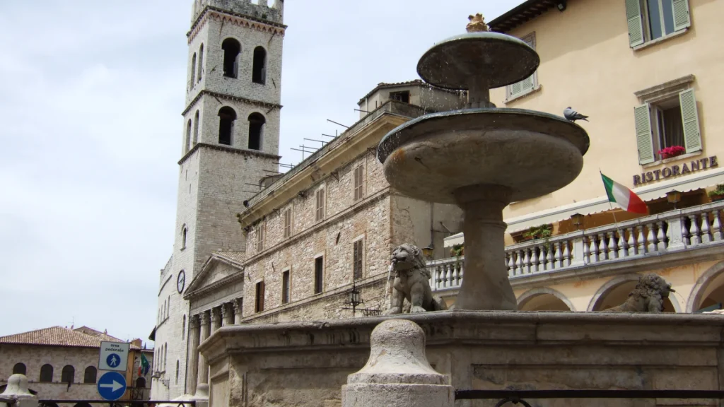 Piazza del Comune [Torre del Popolo, 1305; Tempio di Minerva, sec. I a.C. {Santa Maria sopra Minerva, 1539}; Fonte di Piazza]. Assisi (Pg).